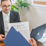 Corretor e cliente analisam documentos de uma solicitação de financiamento imobiliário sobre uma mesa.