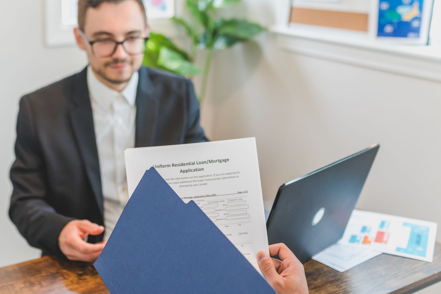 Corretor e cliente analisam documentos de uma solicitação de financiamento imobiliário sobre uma mesa.