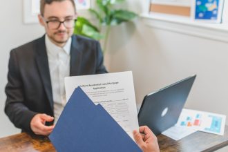 Corretor e cliente analisam documentos de uma solicitação de financiamento imobiliário sobre uma mesa.