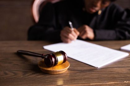 Pessoa assina documentos jurídicos sobre uma mesa, com um martelo de juiz em primeiro plano.