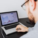 Profissional analisando dados empresariais e gráficos financeiros em um laptop, em ambiente interno.