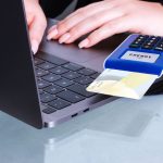 Mãos realizam um pagamento digital com cartão e leitor conectado a um laptop.