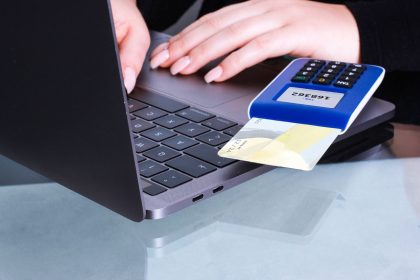 Mãos realizam um pagamento digital com cartão e leitor conectado a um laptop.