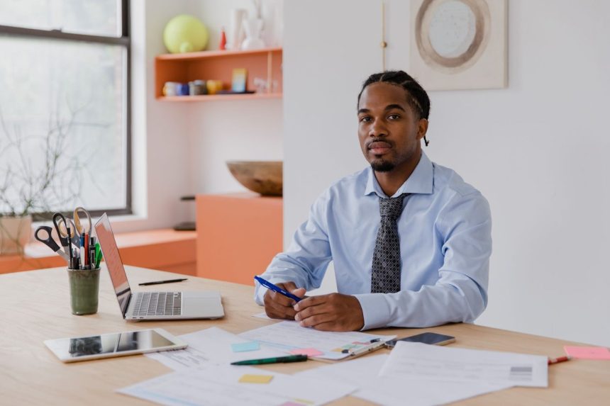 Empreendedor sentado à mesa, trabalhando em um laptop ao lado de documentos.