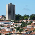 Vista de área residencial de Itapira, no interior de São Paulo, com casas e um edifício alto sob céu azul.