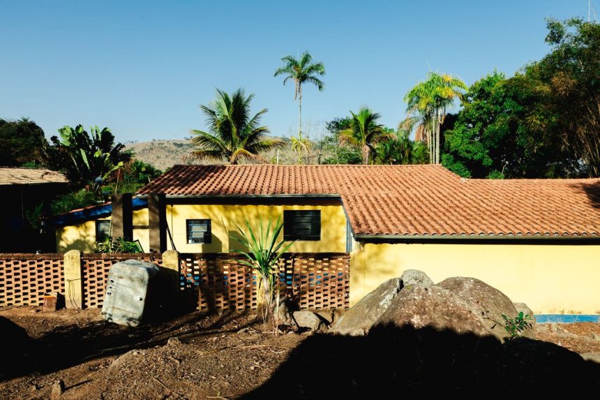 Casa amarela em área rural, cercada por vegetação tropical.