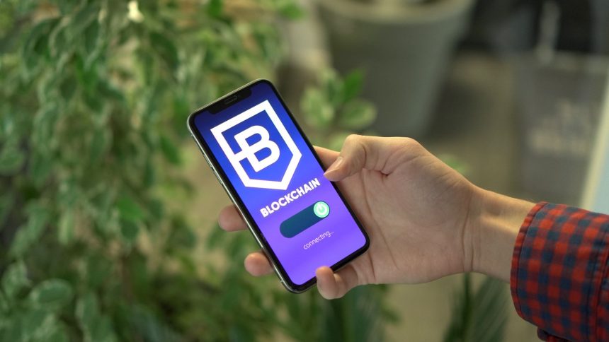 Mão segurando um smartphone com um aplicativo de blockchain exibido na tela.