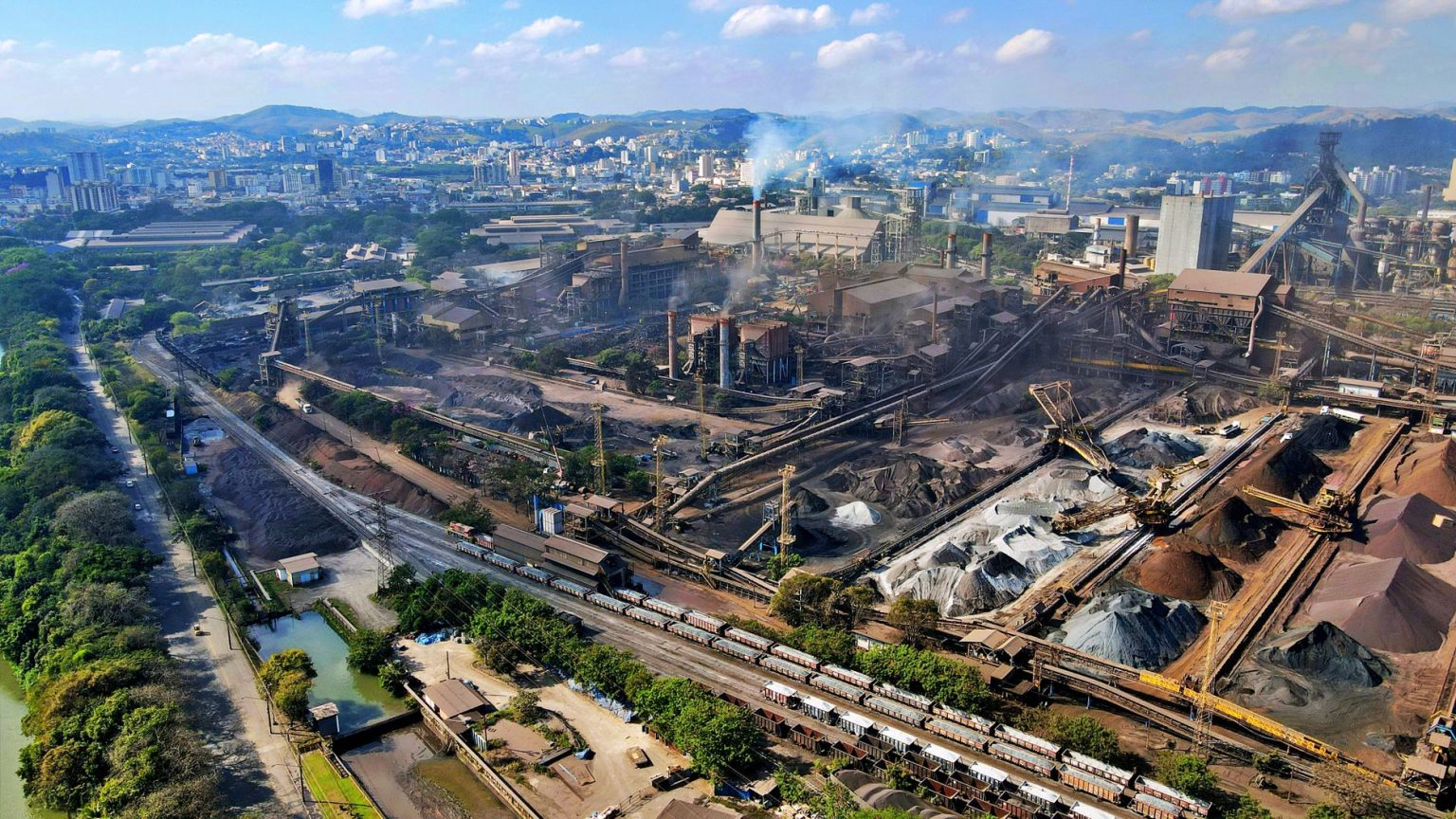 Vista aérea de uma área industrial no Rio de Janeiro, com fábricas e trechos da paisagem urbana.