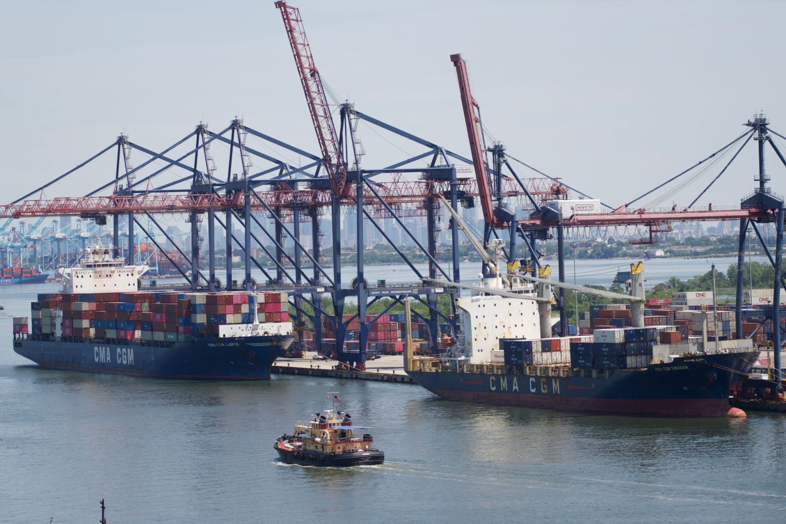 Porto industrial com grandes navios porta-contêineres e guindastes sob céu claro.